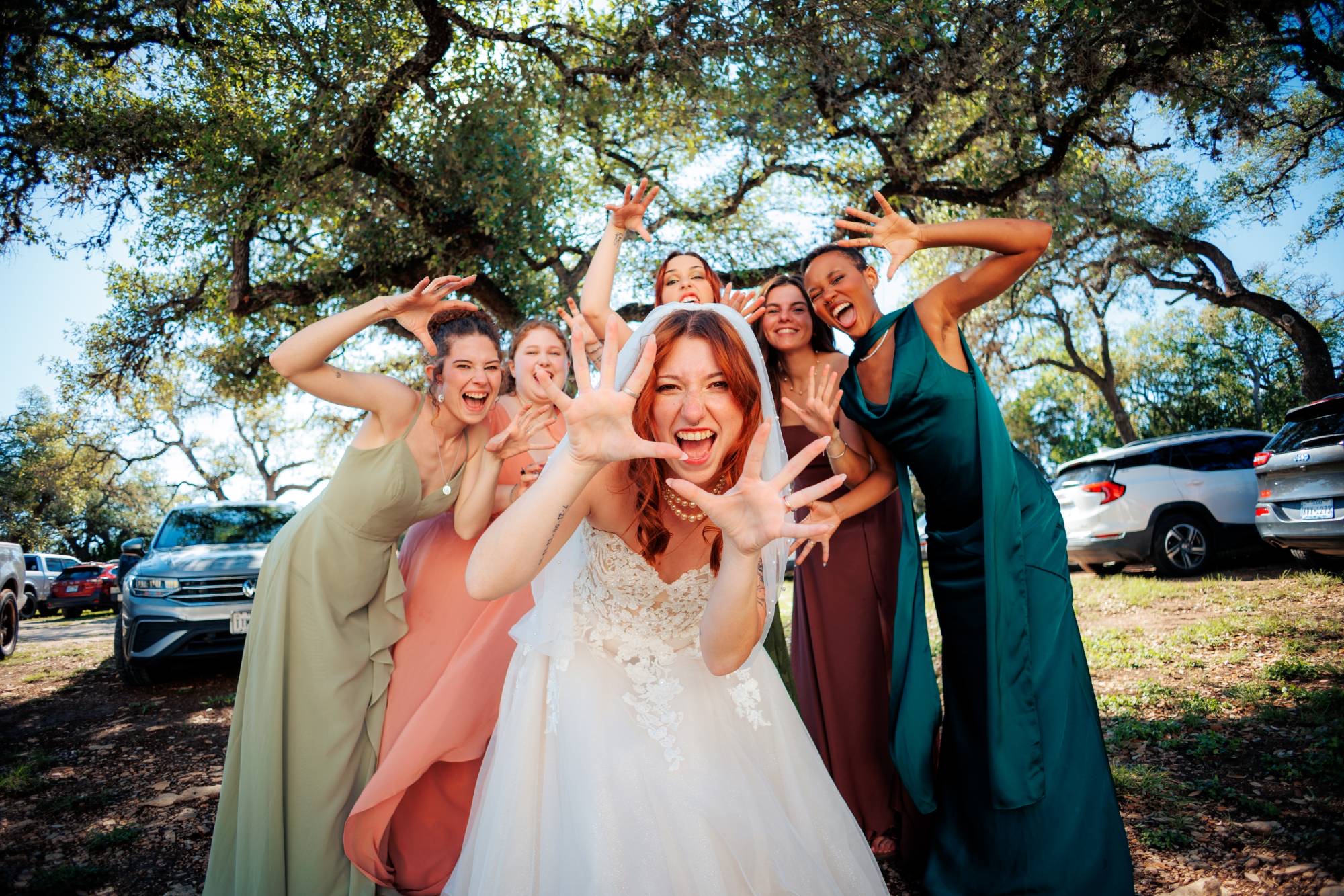 A laughing bride and her bridesmaids pull faces at the camera beneath a live oak
