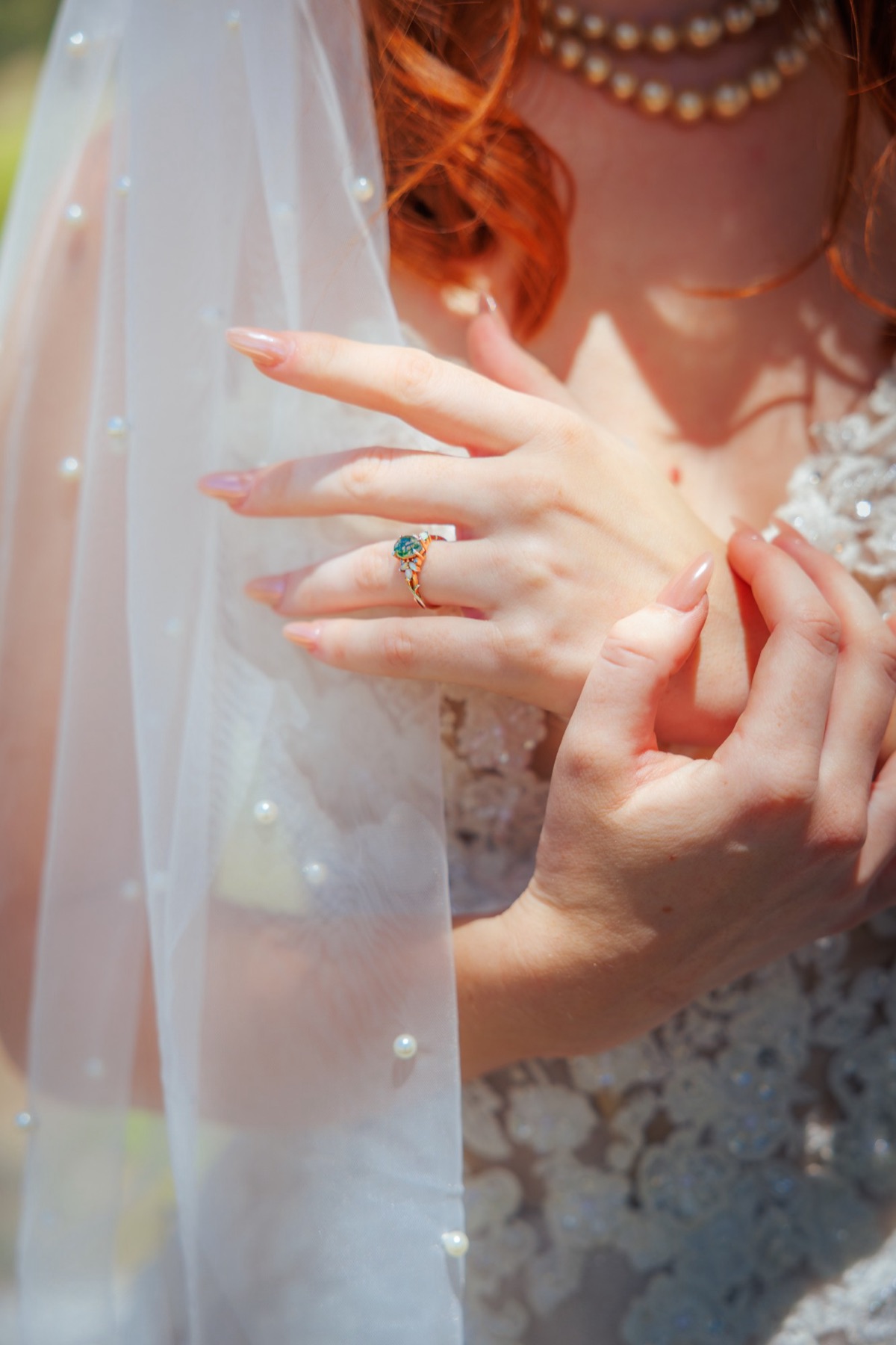 A bride's hands and opal engagement ring beneath a pearl-studded veil