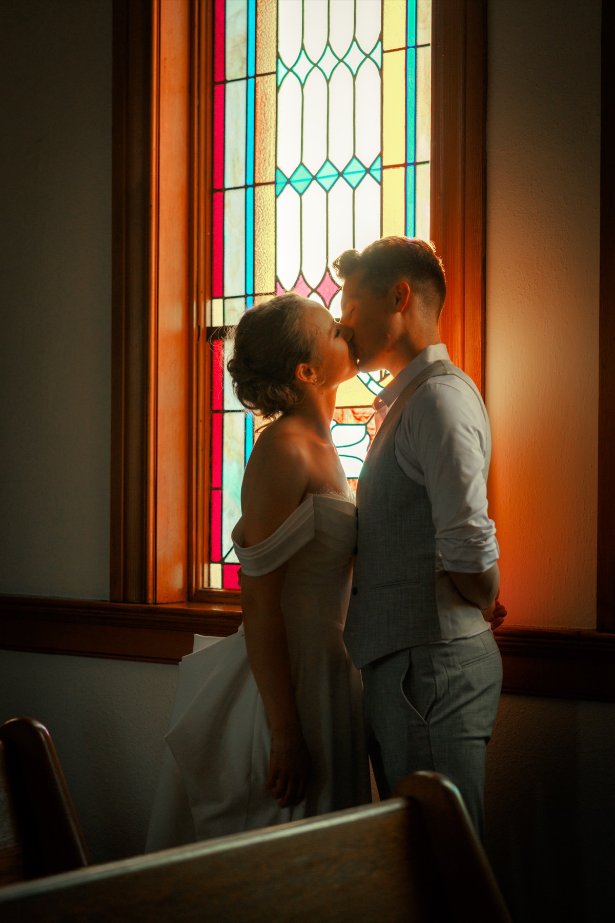 A bride and groom kiss in front of a stained-glass window