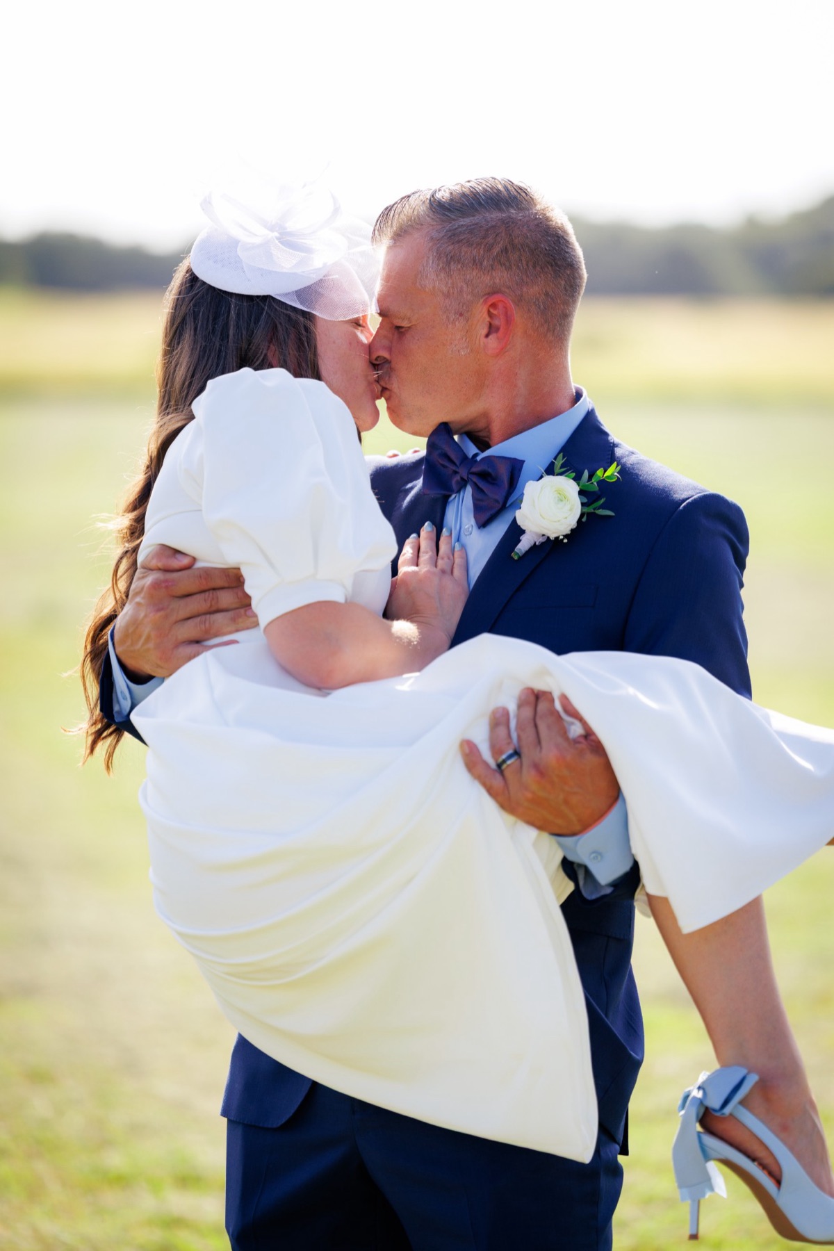 The groom carries his bride and kisses her in the sunlit field